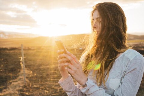 Island, Frau benutzt Smartphone bei Sonnenuntergang, lizenzfreies Stockfoto