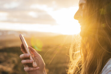 Island, Frau benutzt Smartphone bei Sonnenuntergang - KKAF01096