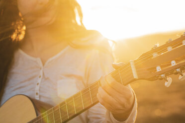 Iceland, woman playing guitar at sunset - KKAF01097