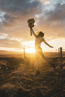 Island, Frau springt mit Gitarre bei Sonnenuntergang - KKAF01099