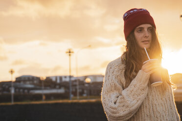 Island, junge Frau mit Kaffee zum Mitnehmen bei Sonnenuntergang - KKAF01114