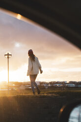 Island, junge Frau mit Kaffee zum Mitnehmen bei Sonnenuntergang, vom Auto aus gesehen - KKAF01121