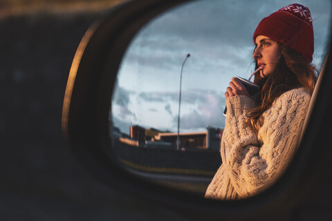 Iceland, young woman with coffee to go at sunset, mirrored in wing mirror stock photo