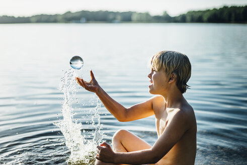 Junge in einem See spielt mit bräunlicher Kugel - MJF02260