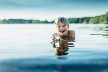 Porträt eines glücklichen Jungen in einem See, der eine durchsichtige Kugel hält - MJF02261