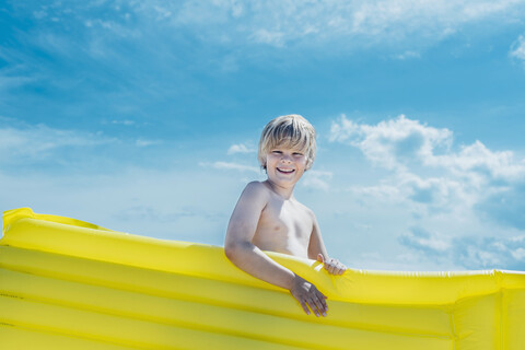 Porträt eines glücklichen Jungen mit einer gelben Luftmatratze im Freien, lizenzfreies Stockfoto