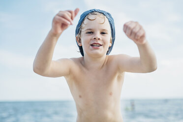 Porträt eines glücklichen Jungen mit einer Mütze am Meer - MJF02285