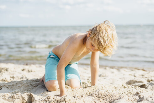 Blond boy playing with sand on the beach - MJF02295