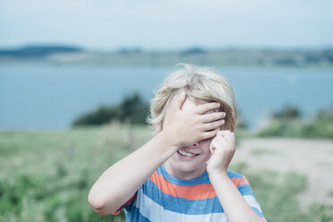 Smiling boy outdoors covering his eyes - MJF02296