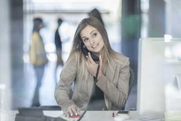 Young businesswoman sitting at desk, using telephone, smiling - ISF06406