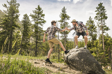 Vater im Wald, hält seinen Sohn an der Hand und hilft ihm auf einen Felsen, Red Lodge, Montana, USA - ISF06410