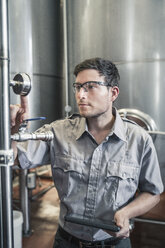 Young man in brewery holding digital tablet checking gauge - ISF06413