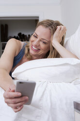 Woman reading smartphone texts in bed - ISF06424