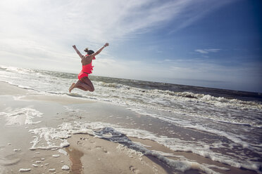 Side view of girl on beach arms raised jumping in mid air - ISF06467