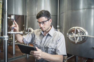 Junger Mann in einer Brauerei, der ein digitales Tablet in der Hand hält und die Anzeige überprüft - ISF06487