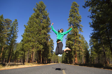 Junge Frau springt mitten in der Luft auf einem Waldweg, Sisters, Oregon, USA - ISF06514