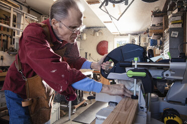 Senior man sawing woodblock in carpentry workshop - ISF06529