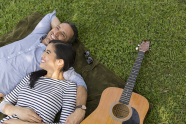 Hoher Blickwinkel auf ein im Gras liegendes Paar mit lächelnder Akustikgitarre - ISF06559