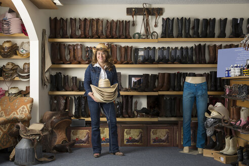 Shop assistant carrying stetsons in front of shelves of boots - ISF06562