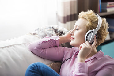 Woman listening with headphones on sofa - CUF17463