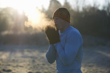 Läufer mit Strickmütze und Handschuhen, reibt die Hände aneinander, atmet kalte Luft - CUF17477