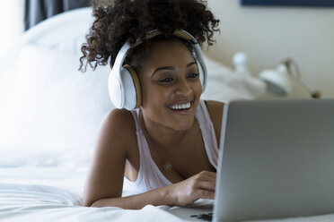 Woman in bedroom, using laptop, wearing headphones - ISF06597