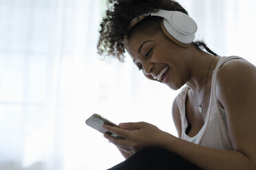 Woman wearing headphones, looking at smartphone, laughing - ISF06598