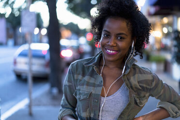 Woman standing in street, wearing earphones, smiling - ISF06601