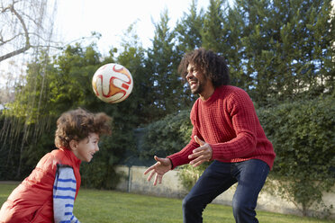 Vater und Sohn spielen lächelnd mit einem Fußball im Garten - CUF17667