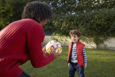 Vater und Sohn spielen lächelnd mit einem Fußball im Garten - CUF17668