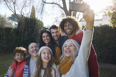 Mehrgenerationenfamilie kauert zusammen und macht mit dem Smartphone ein Selfie, lächelnd - CUF17671