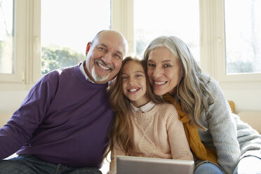 Grandparents on window with granddaughter holding digital tablet looking at camera smiling - CUF17685