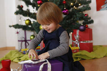 Mädchen vor dem Weihnachtsbaum schaut nach unten und öffnet Geschenke - CUF17707