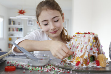 Girl at kitchen counter decorating ginger bread house smiling - CUF17712