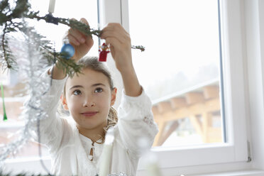 Mädchen mit erhobenen Armen, die Weihnachtsschmuck an den Weihnachtsbaum hängen - CUF17716