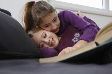 Oberflächenansicht eines Mädchens, das auf dem Sofa liegt und ein Buch liest, sich umarmt und lächelt - CUF17717