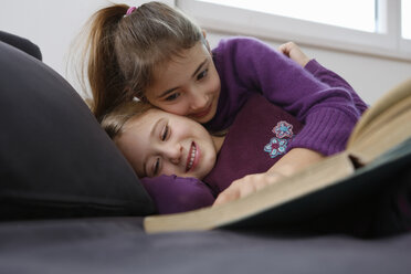 Surface level view of girl lying down on sofa reading book, hugging and smiling - CUF17717