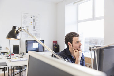 Mid adult man in office using computer hand on chin - CUF17746