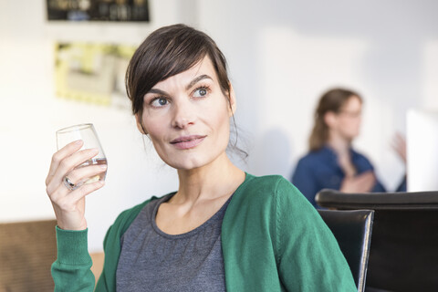 Reife Frau im Büro, die ein Trinkglas hält und wegschaut, lizenzfreies Stockfoto