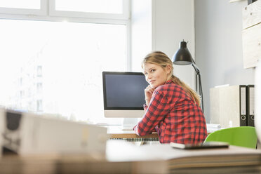 Rückansicht einer jungen Frau am Computer, die lächelnd über die Schulter in die Kamera schaut - CUF17785