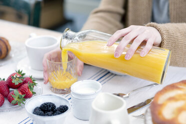 Cropped view of woman pouring orange juice from bottle into glass - CUF17931