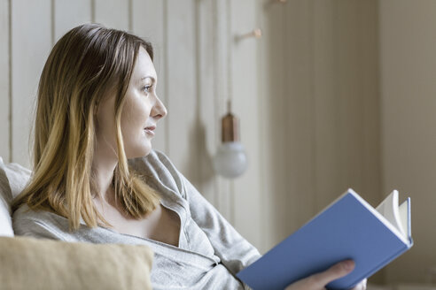 Frau sitzt auf dem Bett und hält ein Buch in der Hand und schaut weg - CUF17942