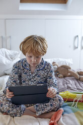 Boy in pyjamas using digital tablet in bed - CUF17976