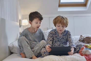 Boys in pyjamas using digital tablet in bed - CUF17977