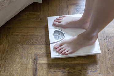 Womans feet standing on bathroom scales - CUF17991
