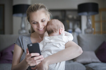 Mutter hält kleinen Jungen, während sie ein Smartphone benutzt - CUF17994