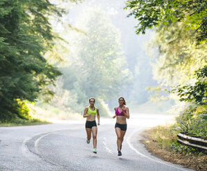 Young woman and teenage girl running along rural road - ISF06685