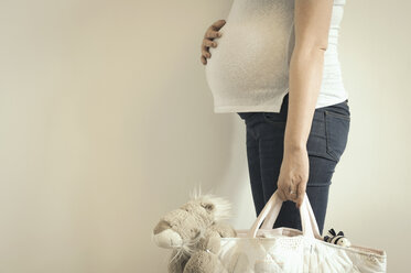 Schwangere Frau, die eine Tasche mit einem Kuscheltier in der Hand hält, Mittelteil - ISF06686