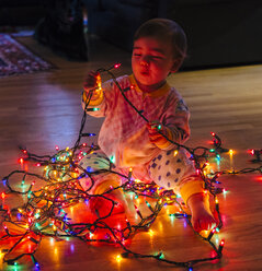 Weibliches Kleinkind spielt mit mehrfarbigen Weihnachtslichtern auf dem Boden - ISF06698