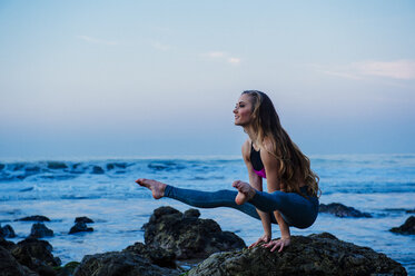 Junge Frau übt Yoga-Pose auf Felsen am Strand, Los Angeles, Kalifornien, USA - ISF06703